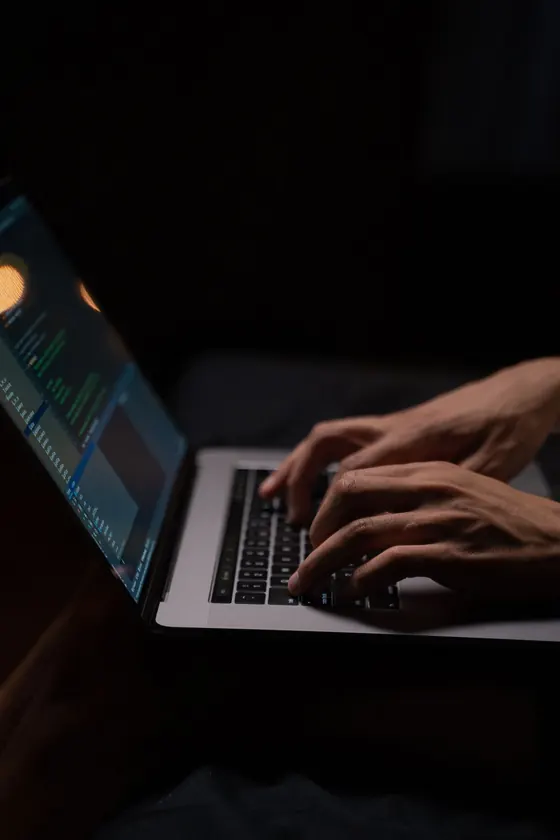 Hands typing on a laptop in a dark room