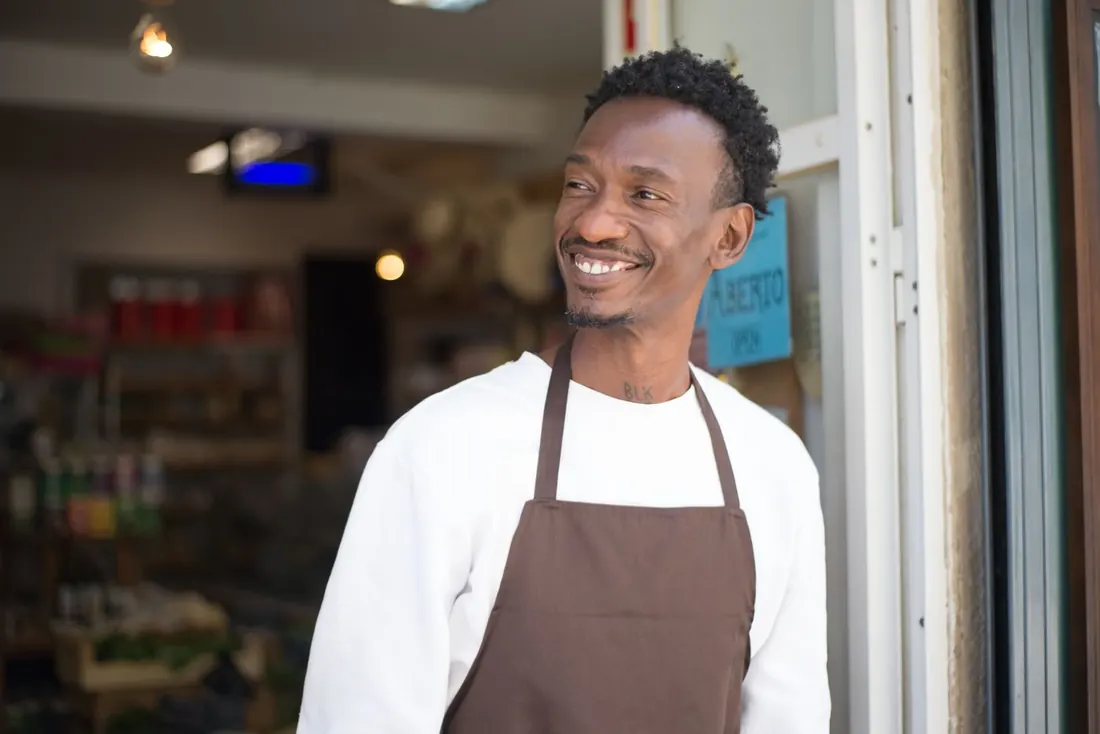 A smiling shop owner in an apron standing in his shop doorway